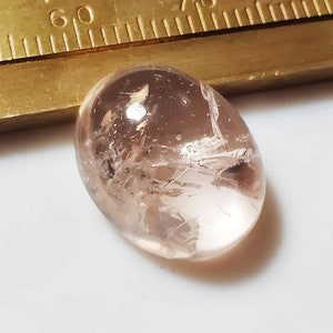 May include: A pale pink oval-shaped gemstone with a cloudy, translucent appearance. The stone has a unique, natural pattern of white inclusions.
