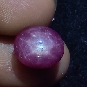 May include: A close-up of a round, pink ruby gemstone with a star-like pattern.
