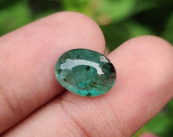 Pode incluir: Uma gema oval verde com inclusões pretas. A gema é lisa e polida.