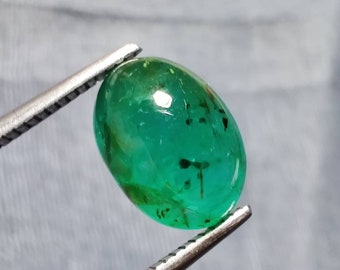 Pode incluir: Uma gema de esmeralda oval verde vibrante com inclusões, segurada por uma pinça.