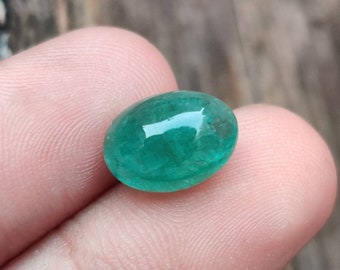 Pode incluir: Uma gema de esmeralda de forma ovalada de cor verde vibrante com uma superfície lisa e polida.