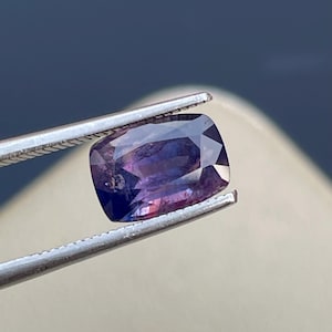 May include: A purple gemstone with a cushion cut, held by tweezers.