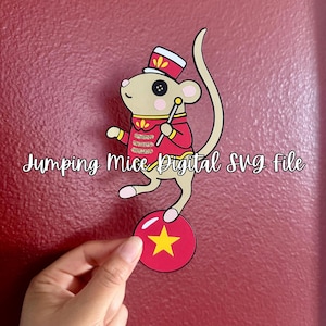 Pode incluir: Um recorte de papel de um rato bege vestido como artista de circo com jaqueta e chapéu vermelhos, segurando um bastão enquanto se equilibra em uma bola vermelha com uma estrela amarela. O texto Jumping Mice Digital SVG file está impresso no centro.