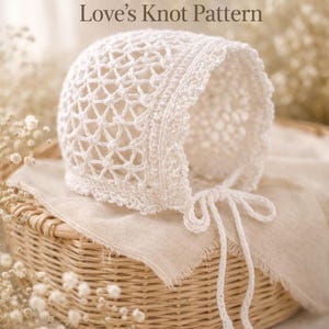 May include: A vintage white baby bonnet with a delicate openwork design, tied with a matching string. The bonnet is displayed on a woven basket with a linen cloth, with the text "Vintage 1915 Heirloom Baby Bonnet Love's Knot Pattern".