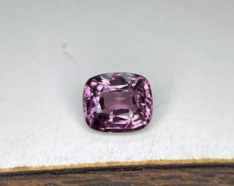 May include: A cushion-cut pink gemstone with a light purple hue.