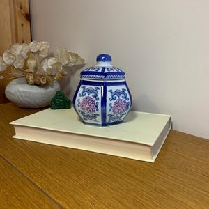 May include: A blue and white ceramic jar with a pink floral design. The jar has a lid and is hexagonal in shape.