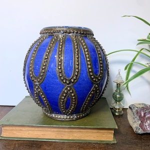 May include: A blue ceramic vase with a gold metal trim and decorative beading. The vase is round and has a wide mouth.