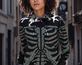 May include: Black zip-up hoodie with a gray skeleton print. The hoodie has a hood and a zipper closure. The model is wearing blue pants.