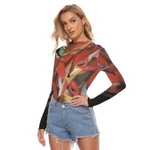 Puede incluir: Una camiseta de manga larga con un dise&ntilde;o abstracto de zorro en tonos rojos, naranjas y verdes. La camiseta tiene un cuello alto y mangas negras. La modelo lleva unos shorts vaqueros.