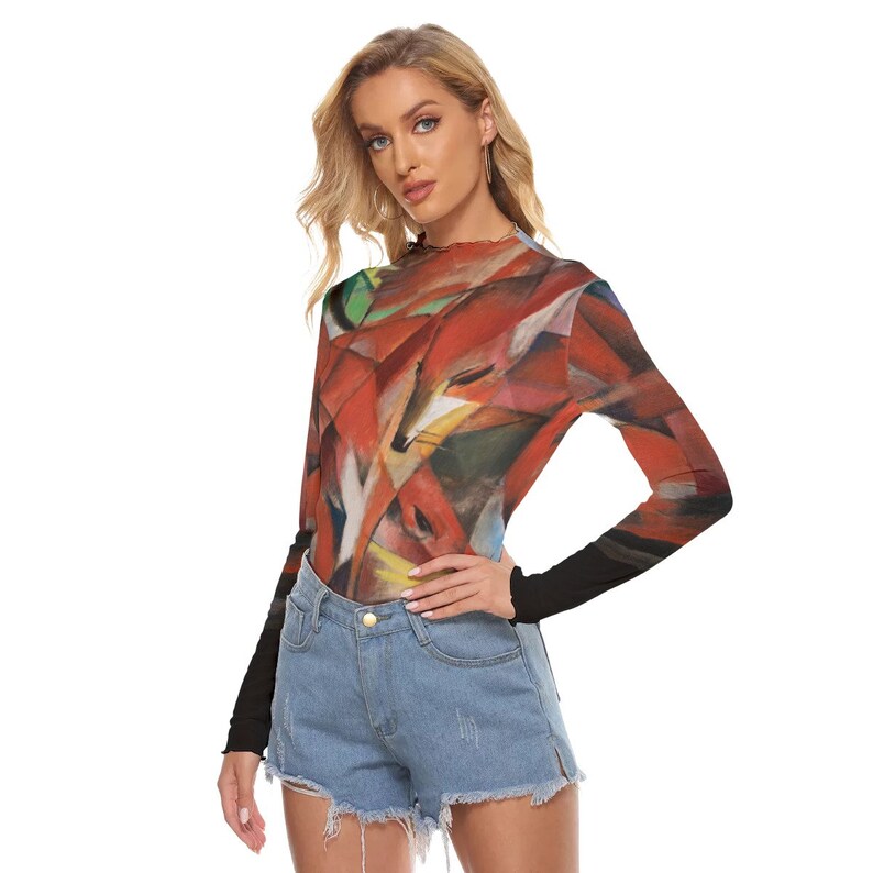 Puede incluir: Una camiseta de manga larga con un dise&ntilde;o abstracto de zorro en tonos rojos, naranjas y verdes. La camiseta tiene un cuello alto y mangas negras. La modelo lleva unos shorts vaqueros.