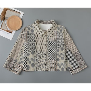 May include: A beige cropped button-up shirt with a patchwork design featuring various geometric and floral patterns in black and brown.