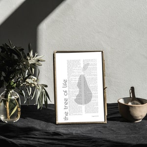 Könnte beinhalten: Ein gerahmter Druck mit einem goldenen Rahmen auf einer schwarzen Oberfläche. Der Druck zeigt eine Silhouette eines Birnbaums mit dem Text "the tree of life", der vertikal auf der linken Seite des Bildes gedruckt ist. Der Text "Genesis 2:9" ist in kleinerer Schrift am unteren Rand des Bildes gedruckt.