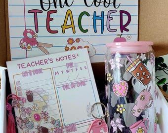May include: A gift box with a teacher theme, containing a jar with a pink lid, a notepad, and a keychain. The jar is decorated with floral and coffee-themed designs. The notepad has a pink tassel and the text "Teacher's Notes". A card with the text "One Cool TEACHER" is also included.