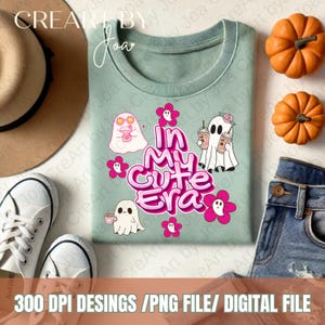 Puede incluir: Una camiseta azul claro con un diseño gráfico rosa y blanco con fantasmas, flores y el texto "In My Cute Era".