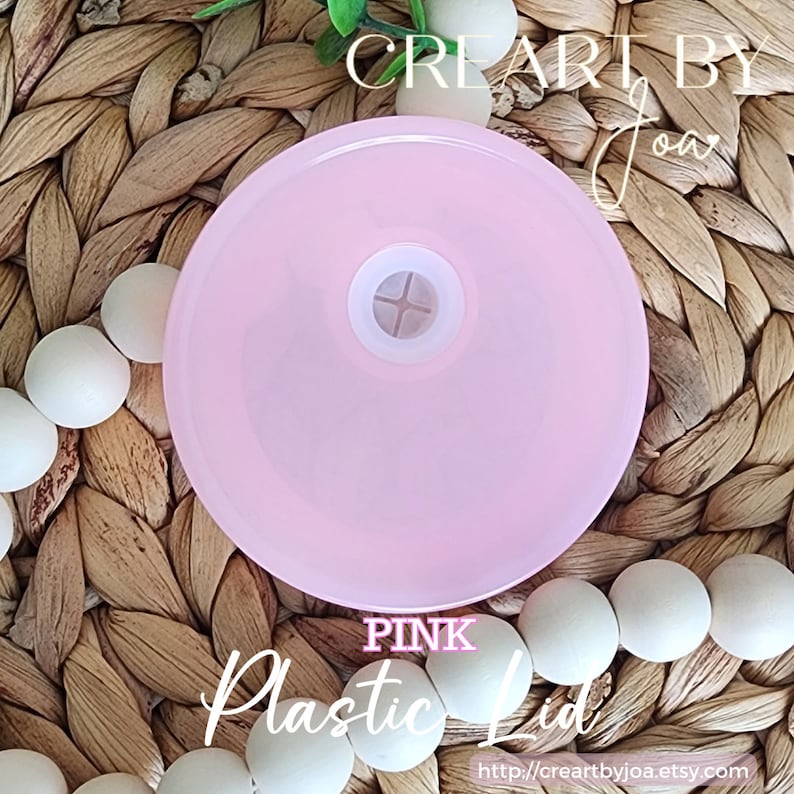 Puede incluir: Tapa de pl&aacute;stico rosa con una peque&ntilde;a pieza central blanca. La tapa est&aacute; sobre una superficie tejida con cuentas blancas.