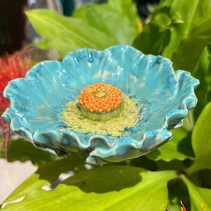 Könnte beinhalten: Eine blumenförmige Keramikschale mit einer glänzenden türkisfarbenen Glasur auf den gewellten Blütenblättern, einer blassgelben Mitte und einer strukturierten, erhabenen orangefarbenen Kuppel in der Mitte. Das Objekt hat eine glatte Oberfläche.