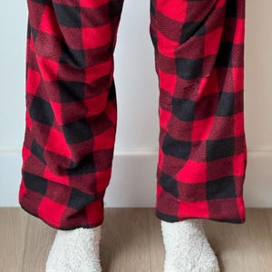 Puede incluir: Pantal&oacute;n de pijama a cuadros rojo y negro con calcetines blancos y peludos.