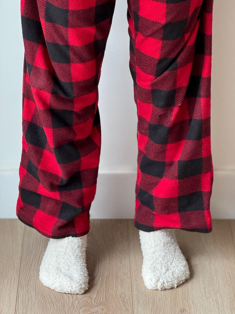 Puede incluir: Pantal&oacute;n de pijama a cuadros rojo y negro con calcetines blancos y peludos.