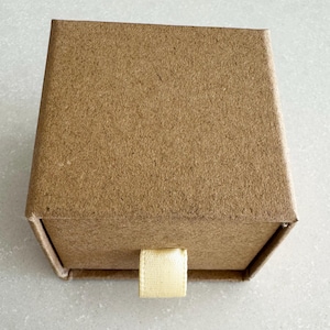 May include: A small, brown cardboard box with a pull-out drawer and a cream-colored fabric pull tab.