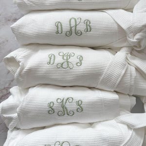 May include: A set of three ceramic mugs with a speckled, matte finish. The mugs are in shades of cream, light brown, and dark brown. Each mug has a simple, minimalist design and a rounded handle.