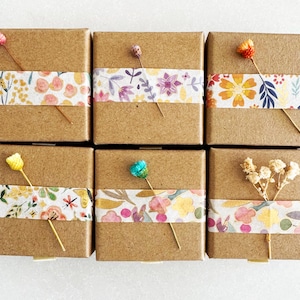 May include: Six small brown cardboard boxes with floral patterned tape. Each box has a small flower or dried flower arrangement on top.