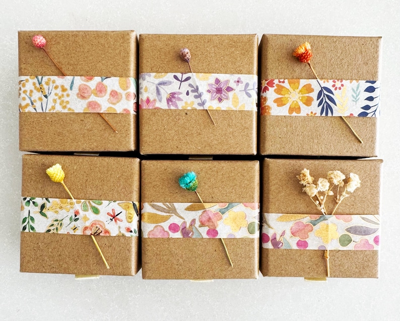 May include: Six small brown cardboard boxes with floral patterned tape. Each box has a small flower or dried flower arrangement on top.