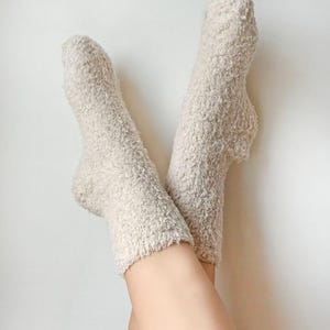 Puede incluir: Un par de calcetines esponjosos de color crema con una textura suave y peluda.