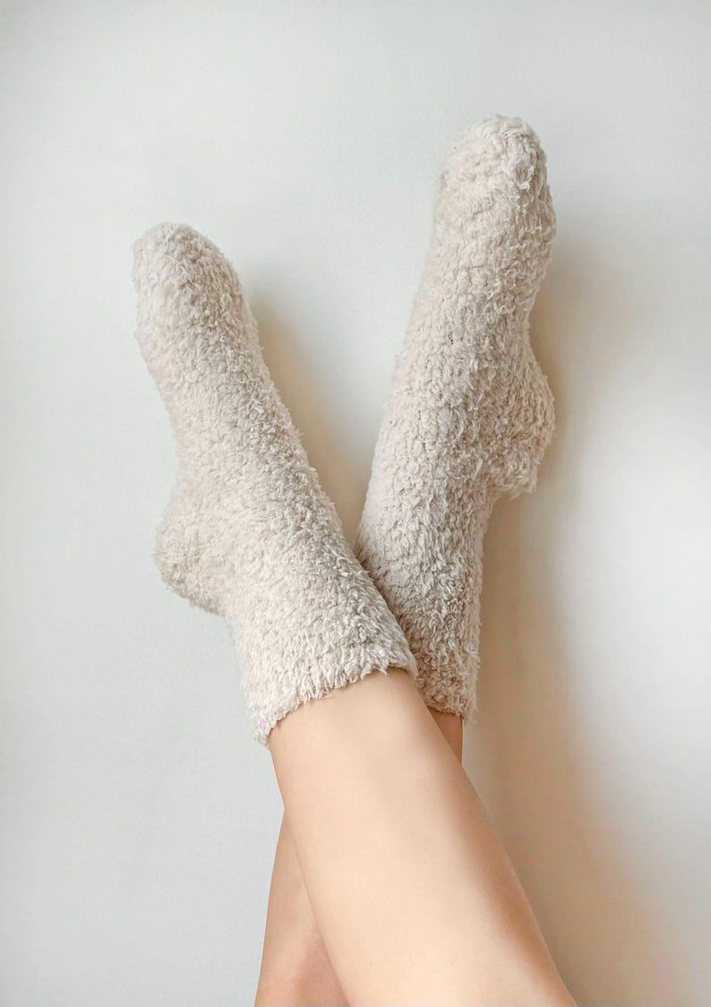 Puede incluir: Un par de calcetines esponjosos de color crema con una textura suave y peluda.