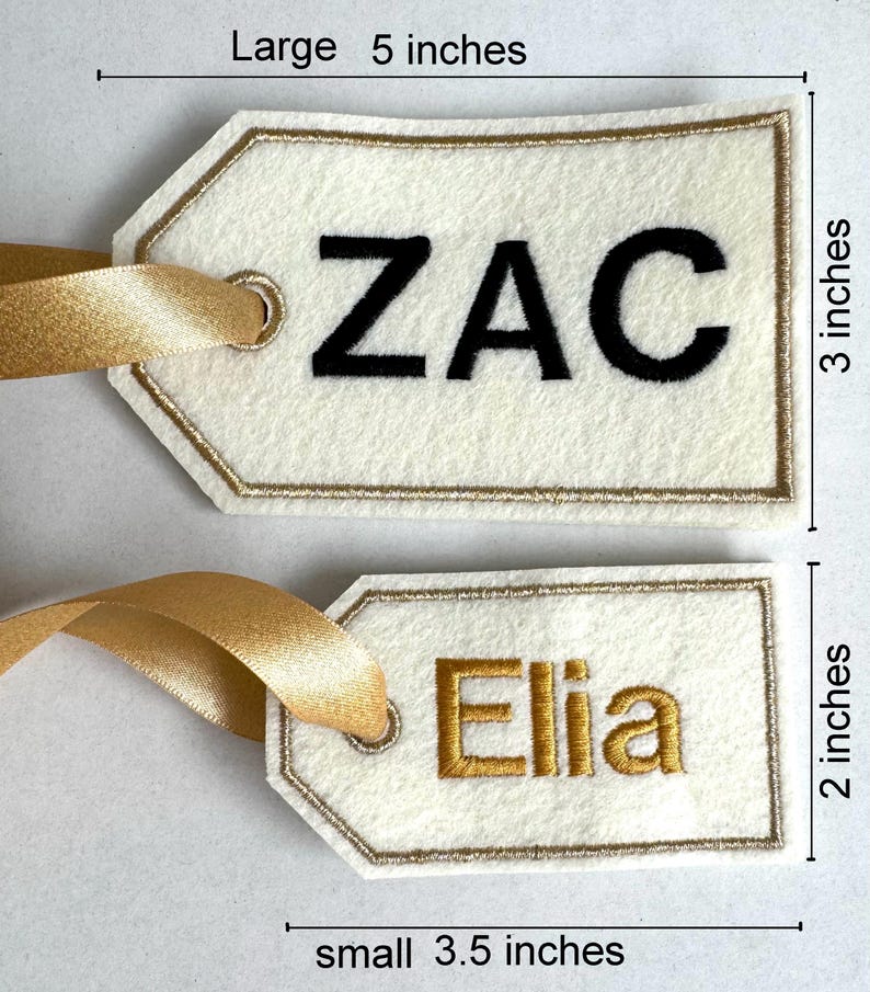 May include: Two personalized gift tags. The larger tag is 5 inches long and 3 inches high, with the name "ZAC" in black. The smaller tag is 3.5 inches long and 2 inches high, with the name "Elia" in gold. Both tags have gold ribbon.