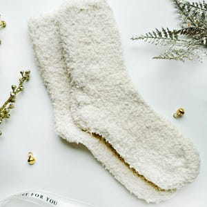 Puede incluir: Un par de calcetines blancos y peludos con el texto "Just For You" en una cinta blanca.