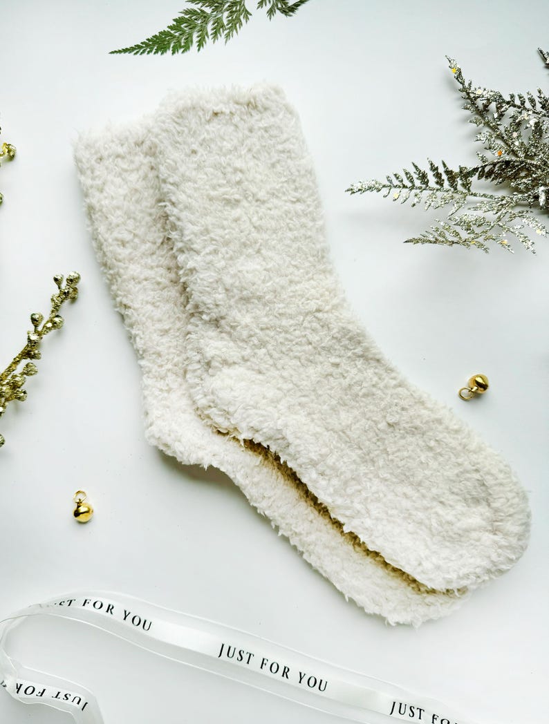 Puede incluir: Un par de calcetines blancos y peludos con el texto "Just For You" en una cinta blanca.