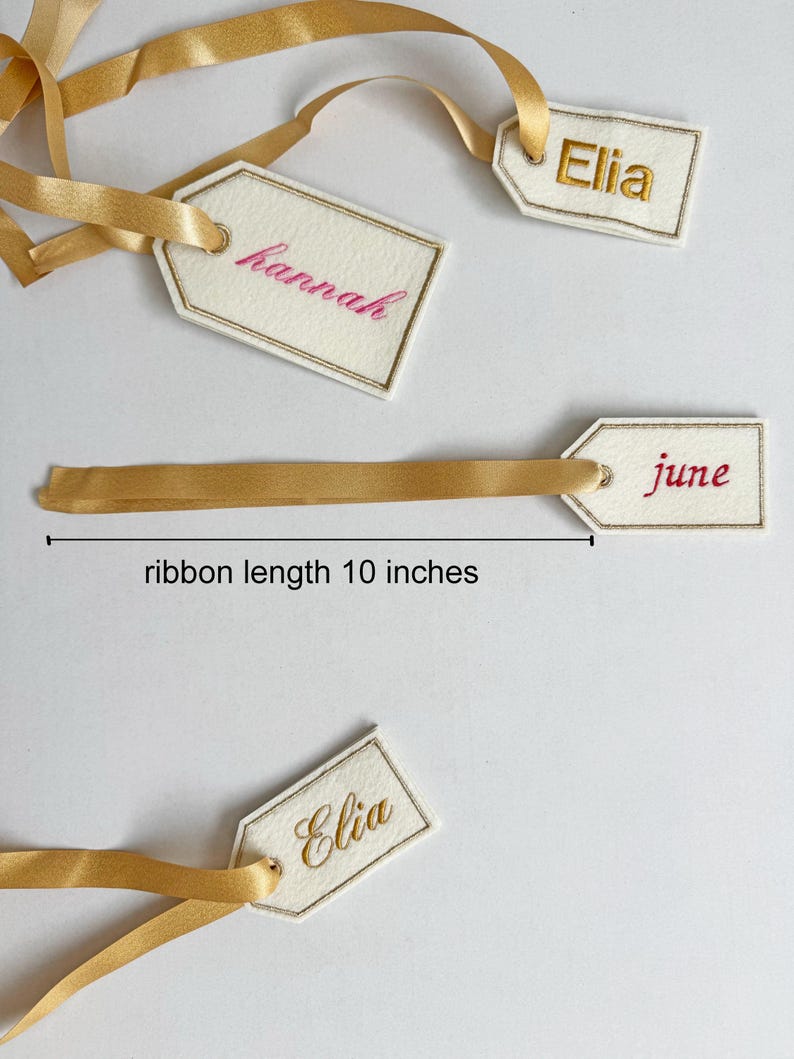 May include: Cream-colored gift tags with gold trim and gold satin ribbons. The tags are embroidered with names in pink and gold thread. The ribbon length is 10 inches.