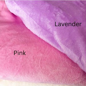 May include: Close-up of two plush fabrics, one pink and the other lavender. The pink fabric is labeled "Pink" and the lavender fabric is labeled "Lavender". The fabrics appear soft and fluffy.