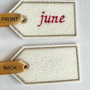 May include: Two off-white felt gift tags with gold trim and ribbon. The front tag has the word "june" embroidered in red. The ribbon says "FRONT" and "BACK".