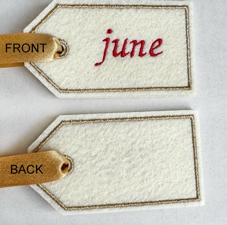 May include: Two off-white felt gift tags with gold trim and ribbon. The front tag has the word "june" embroidered in red. The ribbon says "FRONT" and "BACK".