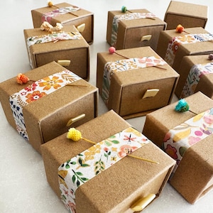 May include: A collection of small, brown cardboard boxes with drawers. Each box is decorated with colorful floral patterned tape and a small flower accent.