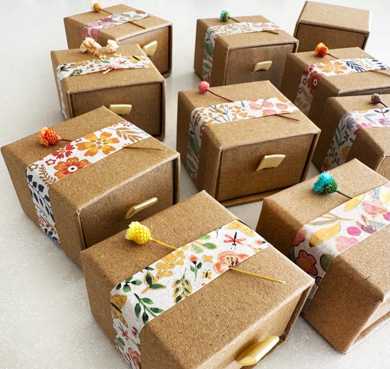 May include: A collection of small, brown cardboard boxes with drawers. Each box is decorated with colorful floral patterned tape and a small flower accent.