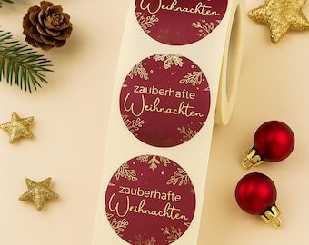May include: A roll of round Christmas stickers with the text "zauberhafte Weihnachten" in gold script on a burgundy background. The stickers have a gold snowflake and floral design. Christmas ornaments and gold stars are scattered around the roll.
