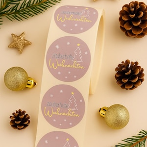 May include: A roll of round stickers with the text "zauberhafte Weihnachten" in gold script, featuring a Christmas tree design. The image also includes gold star ornaments, pine cones, and evergreen sprigs, creating a festive holiday theme.