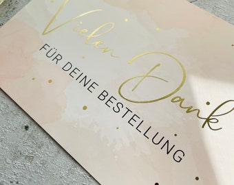May include: A pink and white card with gold foil lettering that says "Vielen Dank" and "FÜR DEINE BESTELLUNG".