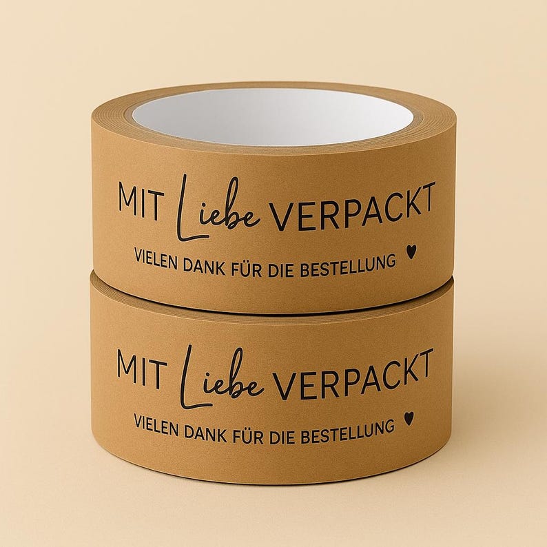以下が含まれることがあります： 茶色の梱包用テープが2巻、重ねられています。「MIT Liebe VERPACKT」と「VIELEN DANK F&Uuml;R DIE BESTELLUNG」という文字が黒い筆記体で印刷されています。小さなハートのシンボルも付いています。