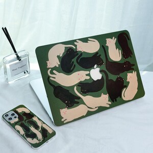 May include: A green laptop case and phone case featuring a pattern of black and cream-colored cat illustrations. The laptop case is open, revealing a white Apple logo. A clear glass bottle with black reeds is also visible.
