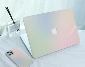 May include: A laptop and smartphone with a pastel rainbow gradient design. The laptop has a silver Apple logo. A clear glass diffuser with black reeds and a label that reads "Mose Fragrance" is also visible.