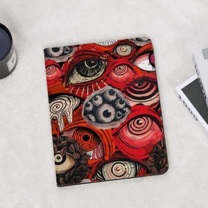 Pode incluir: Uma capa de caderno retangular, vermelha e preta, com um padrão repetido de olhos estilizados em vários tamanhos e estilos. O design inclui um grupo de olhos pequenos e cinzentos e outras formas abstratas.