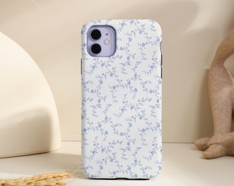 Könnte beinhalten: Eine weiße Handyhülle mit einem blauen Blumenmuster. Die Hülle hat einen Kameraausschnitt und ist für ein Smartphone konzipiert.