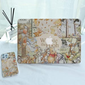 Op de afbeelding: Een laptophoes en telefoonhoesje met een Winnie the Pooh-ontwerp. De hoesjes hebben een beige achtergrond met illustraties van Pooh, Teigetje, Knorretje en Iejoor. De laptophoes heeft de tekst "Winnie the Pooh".