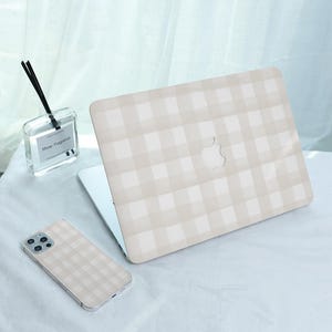 May include: A laptop and a smartphone, both featuring a beige and white gingham pattern. The laptop has the Apple logo. A clear glass diffuser with black reeds is in the background.