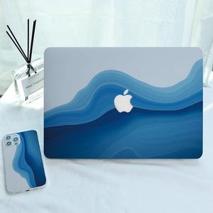 May include: A laptop and phone case featuring a blue wave pattern. The laptop displays a white Apple logo. The phone case mirrors the design. The colour scheme incorporates various shades of blue and white.