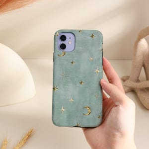 May include: A sage green phone case featuring a repeating pattern of gold-colored stars and crescent moons. The case has a textured surface and a cutout for a dual-lens camera system with a light purple camera module housing.