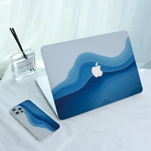 May include: A laptop and a smartphone, both with a blue wave design. The laptop has a white Apple logo. The phone and laptop cases have a gradient of blue hues. A clear glass bottle with black reeds is in the background.